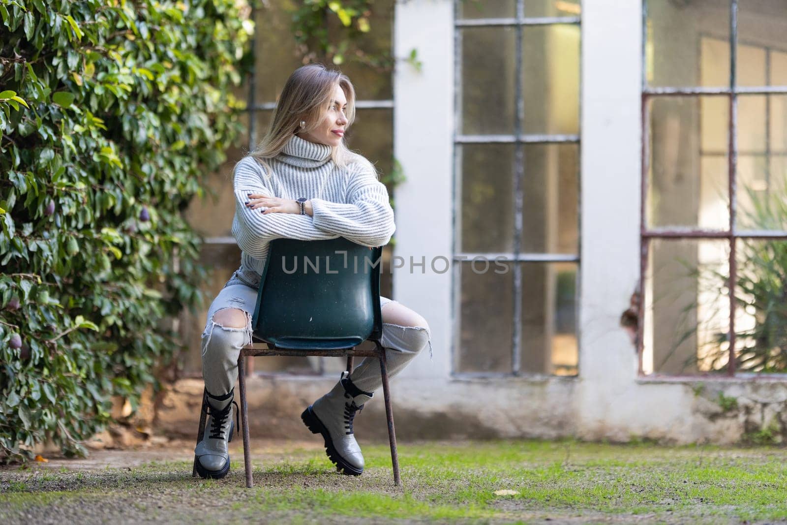 Young woman is sitting on a chair in a garden, looking away from the camera