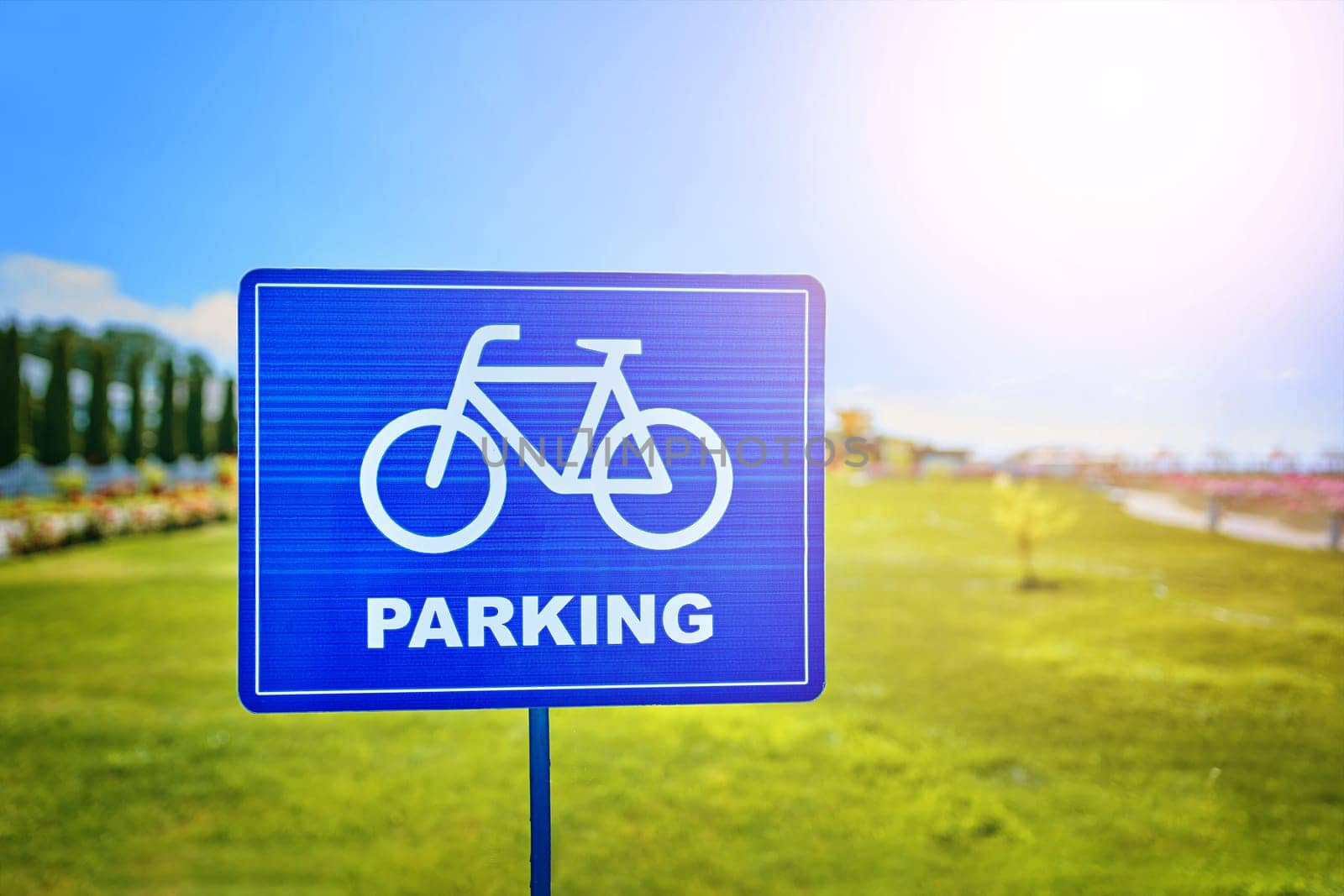 A blue rectangle traffic sign with a bicycle wheel symbol and the word parking in a skyblue font, set against a natural landscape backdrop