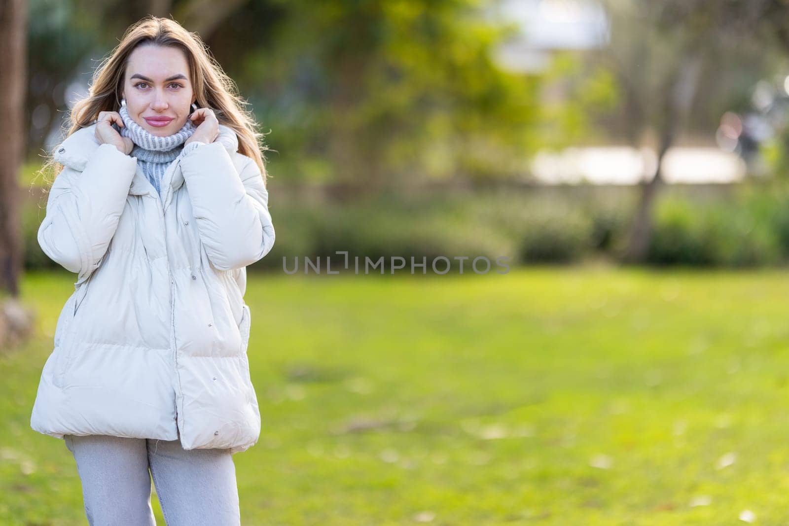 Young woman is bundling up in her warm winter clothes on a sunny but cold day in the park