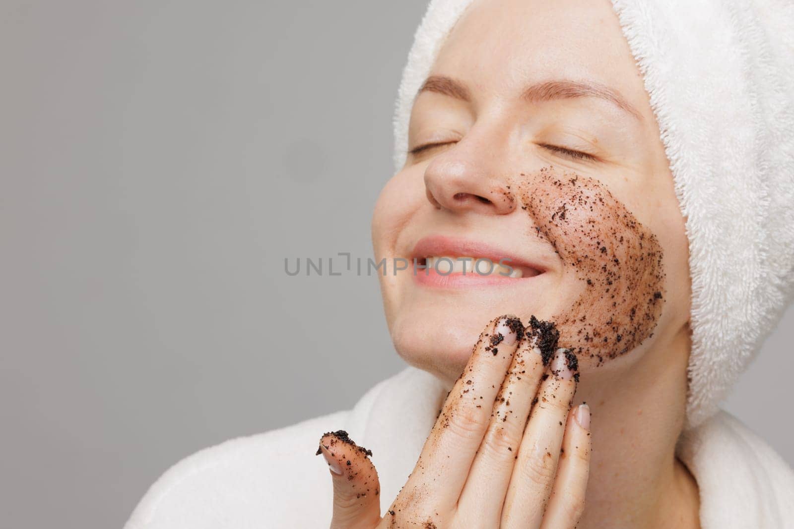 Woman enjoying facial skin care, applying black coffee face scrub, concept of rejuvenation and facial skin care
