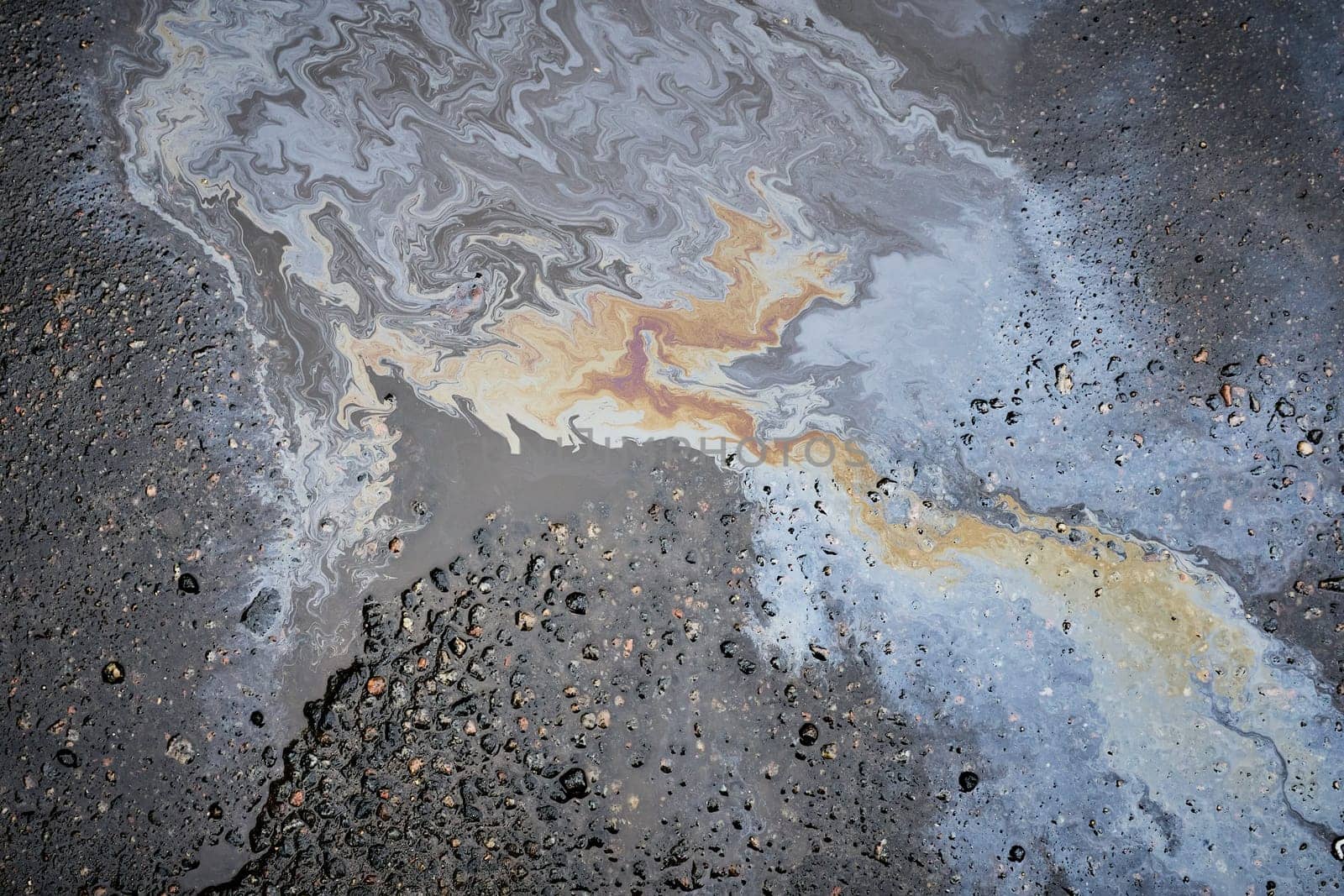 A close-up of a shiny fuel spill on wet pavement, shot from above