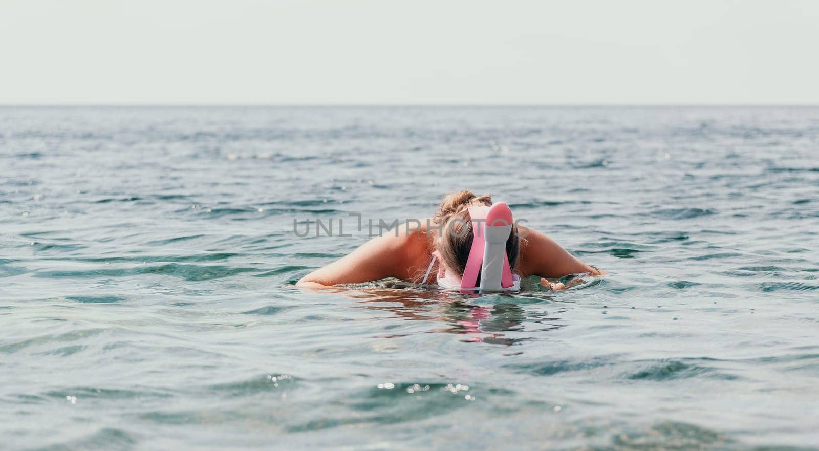 Young happy woman in white bikini put pink snorkeling mask on beach before swimming. girl having fun relaxing on beautiful beach. Beach lifestyle