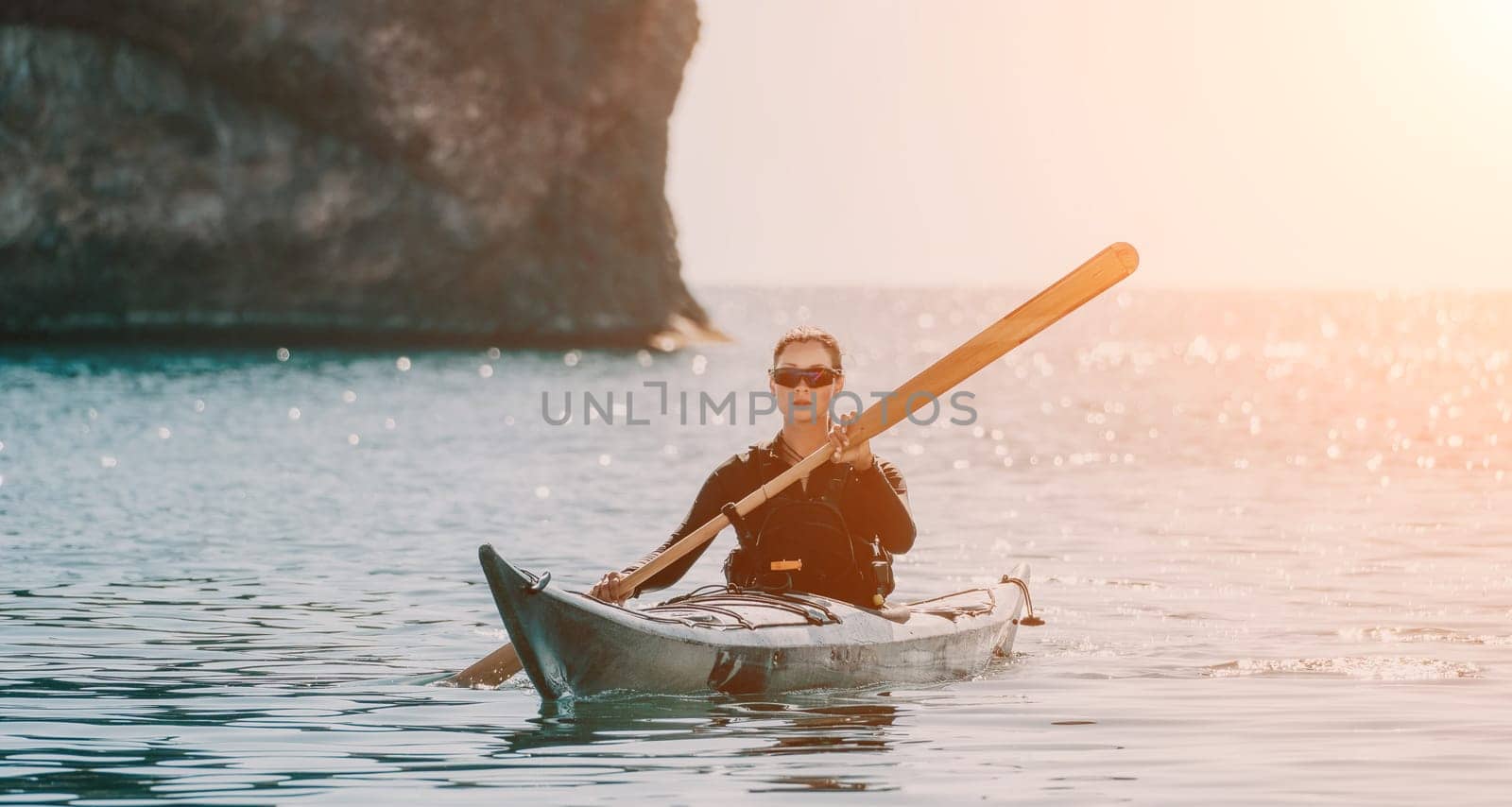 Happy smiling woman in kayak on ocean, paddling with wooden oar. Calm sea water and horizon in background