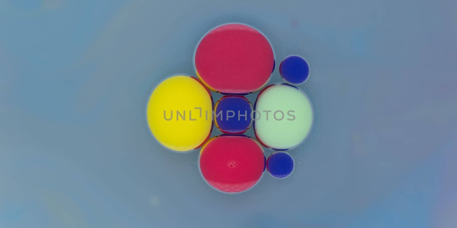 A vibrant collection of spherical shapes in red, yellow, blue, and green floats gracefully against a soft blue backdrop. The colors create a striking visual contrast and harmony.