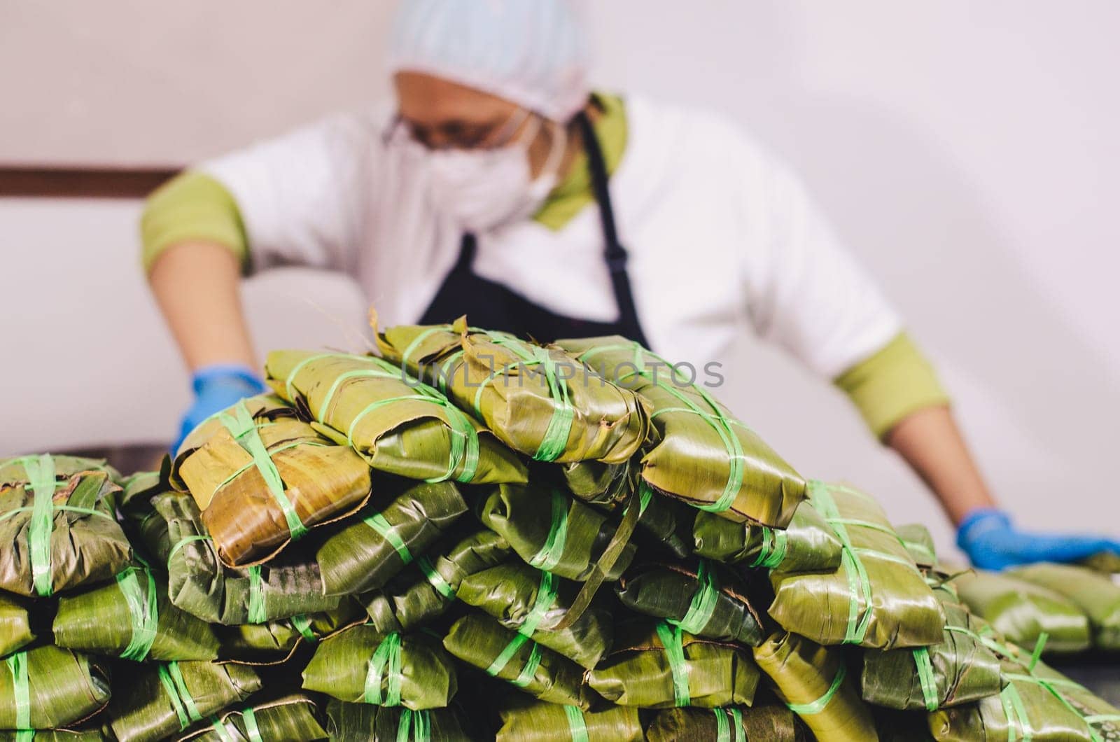 Stack of tamales with unrecognizable woman in the background preparing the Peruvian tamales