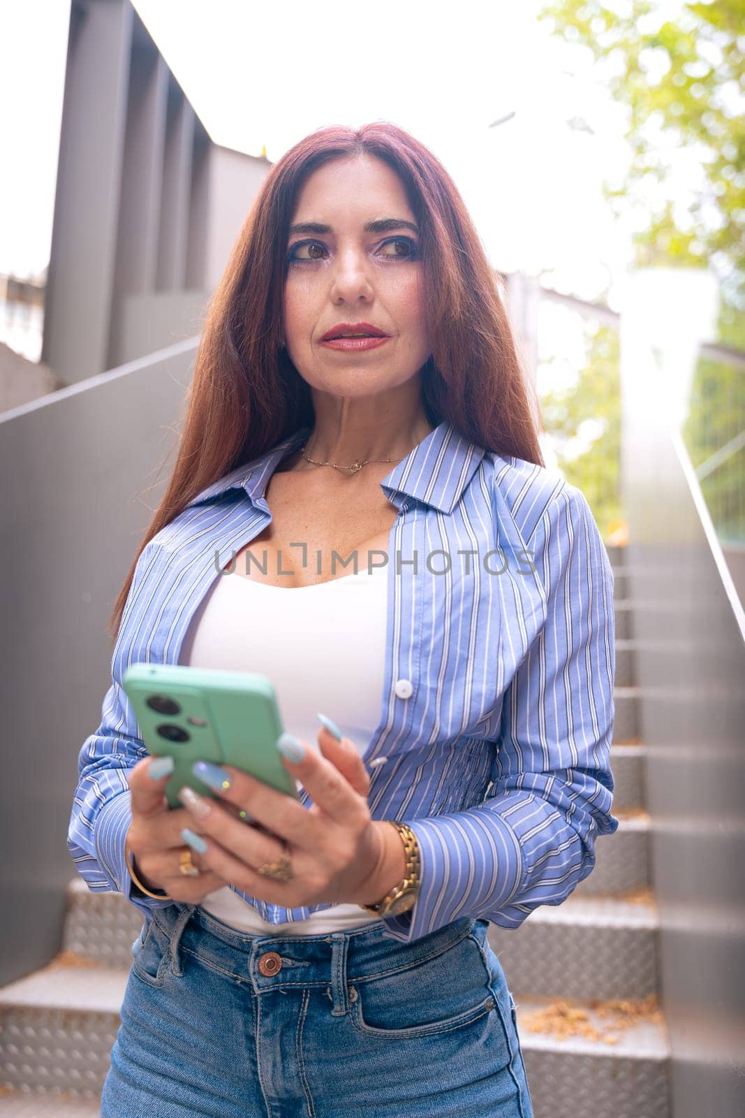 Woman wearing sunglasses with cell phone in hands, writes messages and reads news online, using an app looking at camera.