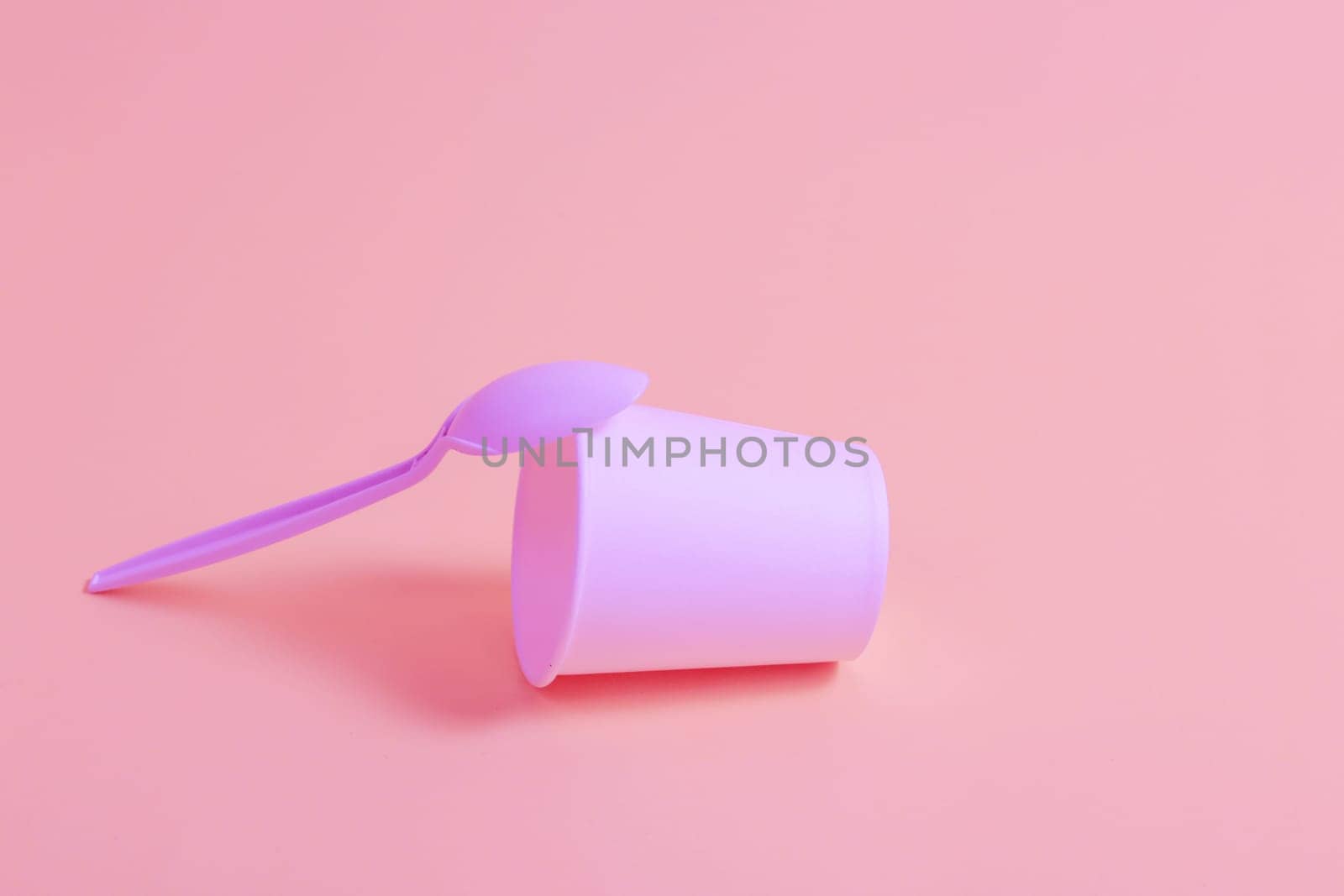 Paper disposable glass and plastic spoon on a pink background. Disposable tableware concept.