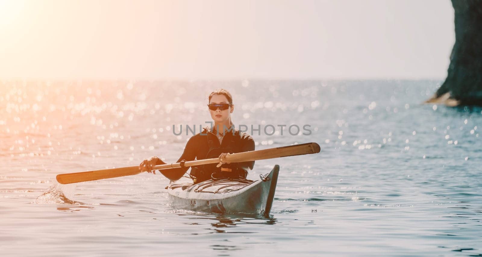 Happy smiling woman in kayak on ocean, paddling with wooden oar. Calm sea water and horizon in background