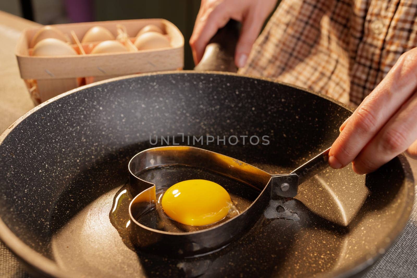 close-up of female hands holding a heart shape on a frying pan with a broken egg, heart-shaped fried egg