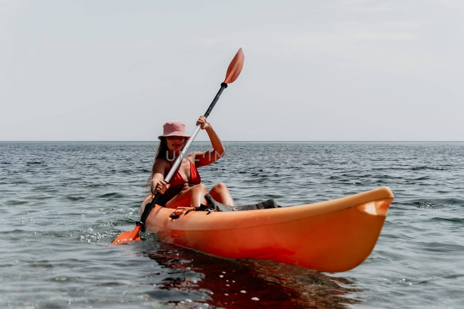 Happy smiling woman in kayak on ocean, paddling with wooden oar. Calm sea water and horizon in background