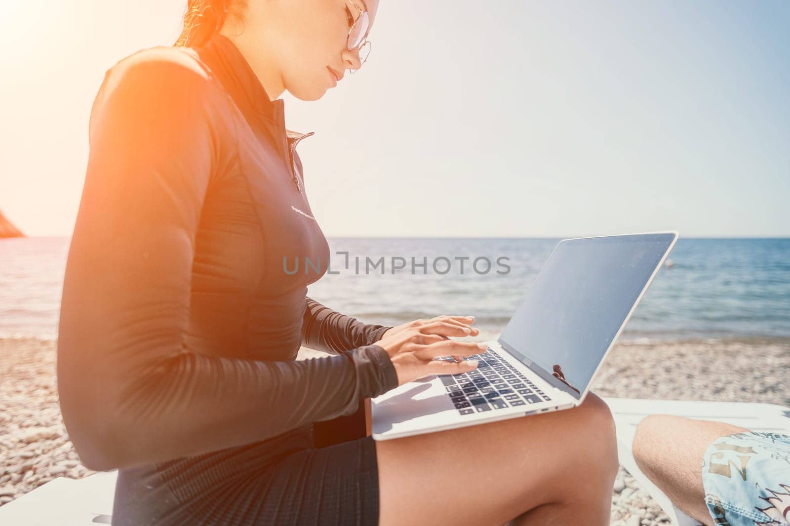 Digital nomad, Business man working on laptop by the sea. Man typing on computer by the sea at sunset, makes a business transaction online from a distance. Freelance, remote work on vacation