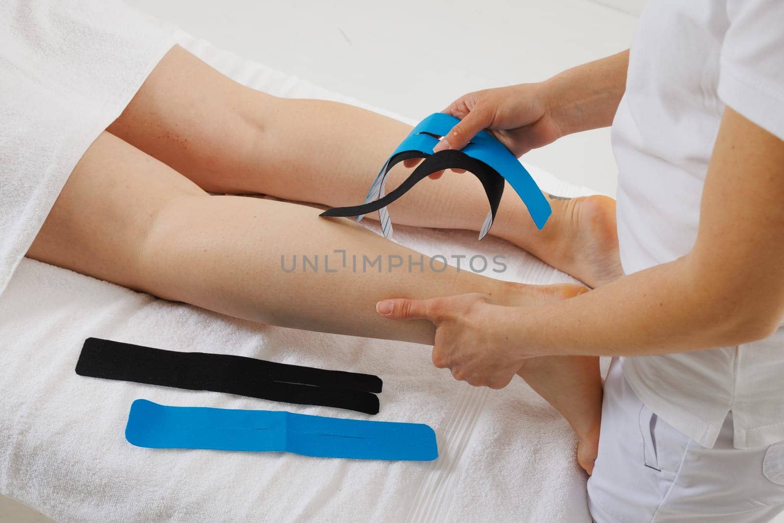 Kinesio taping of the lower extremities to prolong the massage effect close-up, the therapist applies tape to the patient's legs
