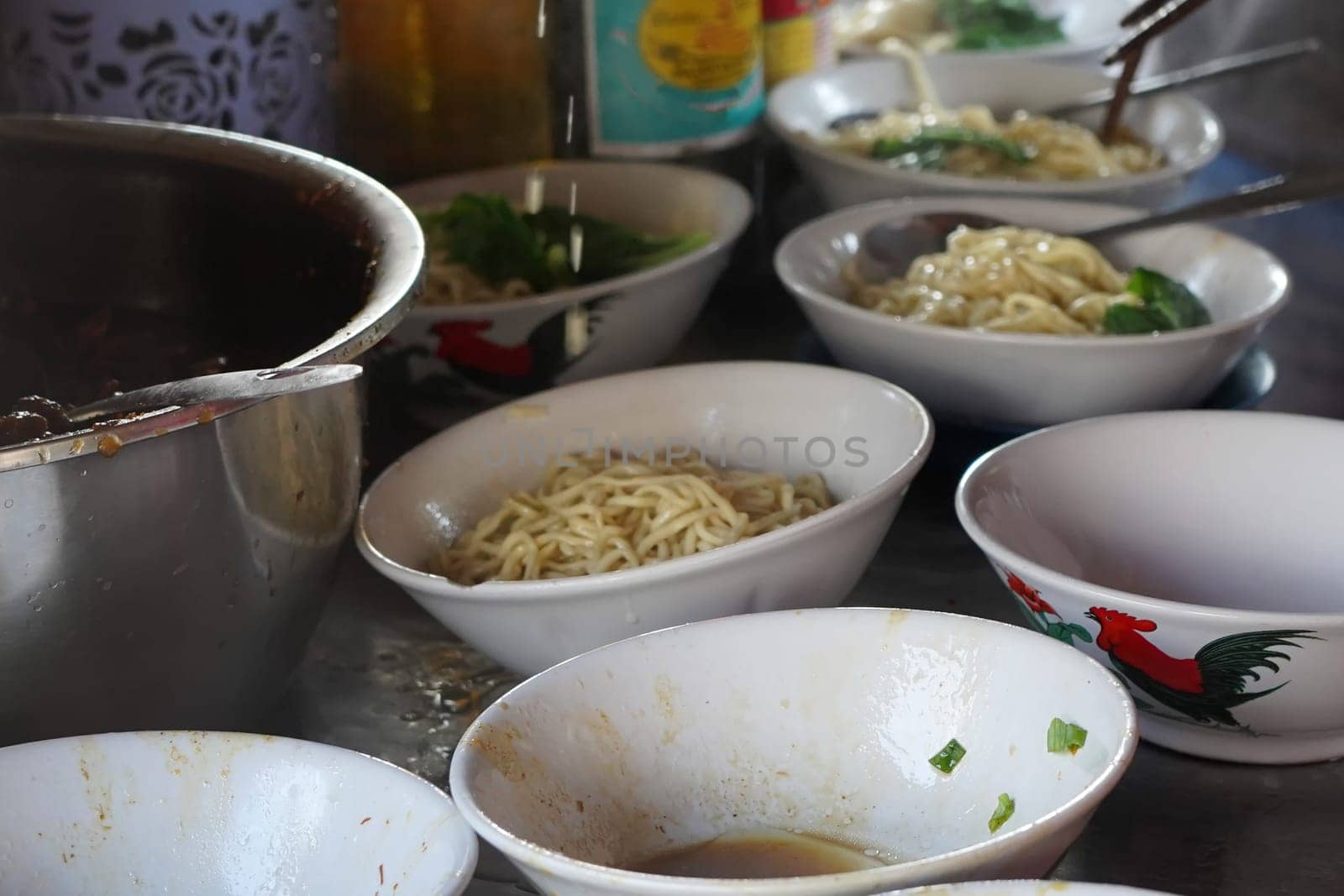 A close-up shot of Tukang Mie Ayam or a noodle vendor preparing multiple servings of chicken noodle soup.