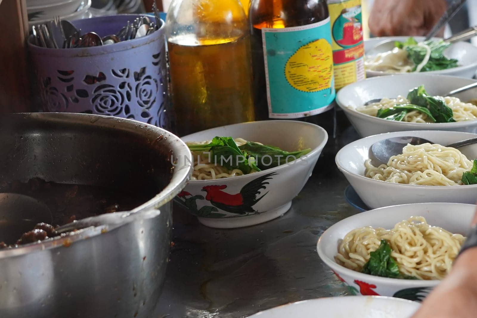 A close-up shot of Tukang Mie Ayam or a noodle vendor preparing multiple servings of chicken noodle soup.