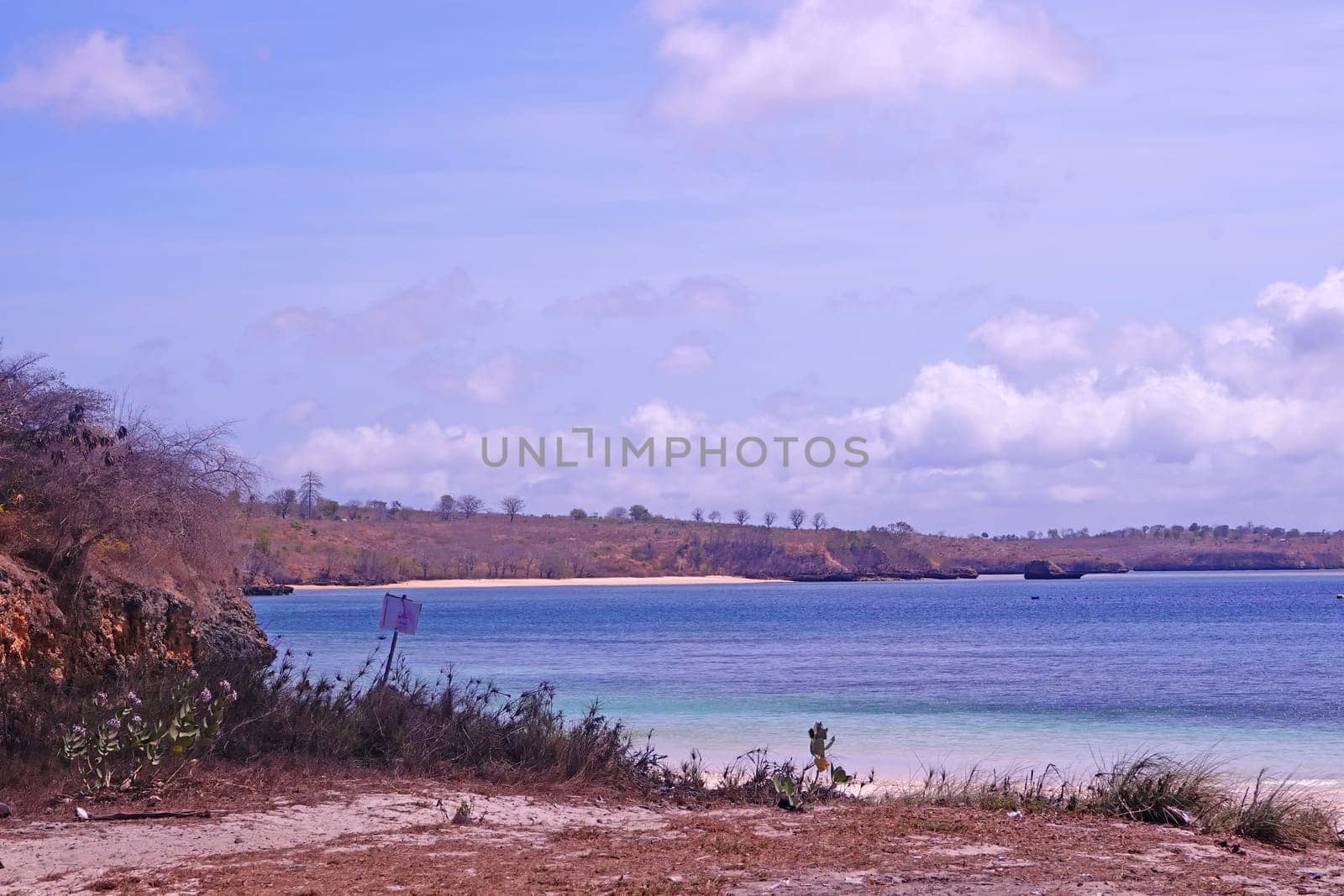 scene of a pristine beach near Pink Beach in Lombok, Indonesia. Clear turquoise waters lap against the white sandy shore, while colorful fishing boats bob gently in the bay