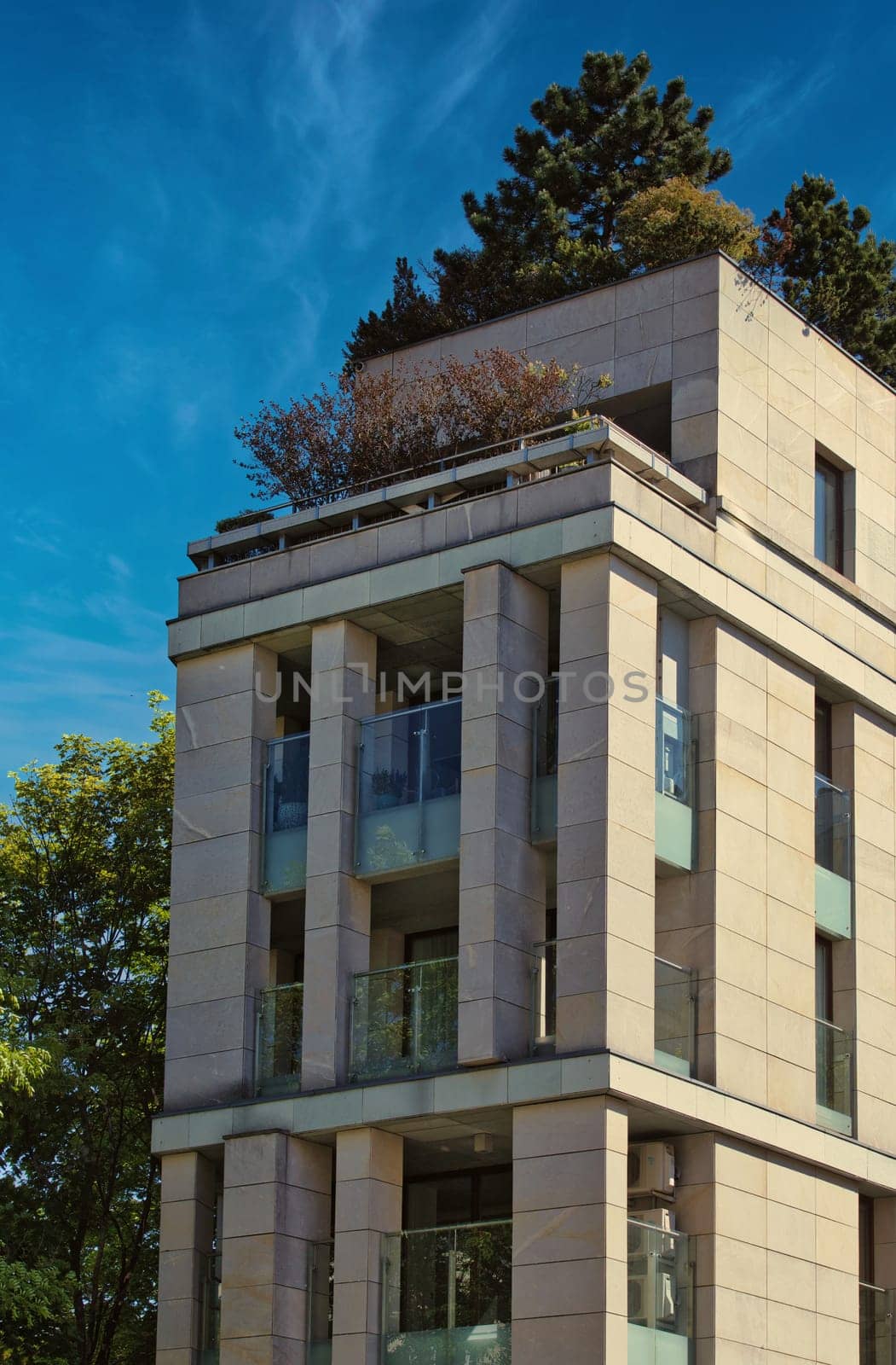A beautiful image of a modern building in Poznan, Poland, featuring clean lines and a rooftop garden. The design blends contemporary architecture with nature, as trees and plants adorn the top of the structure. Captured against a bright blue sky, this image showcases urban development that integrates sustainability. Perfect for themes related to architecture, urban design, and eco-friendly construction.