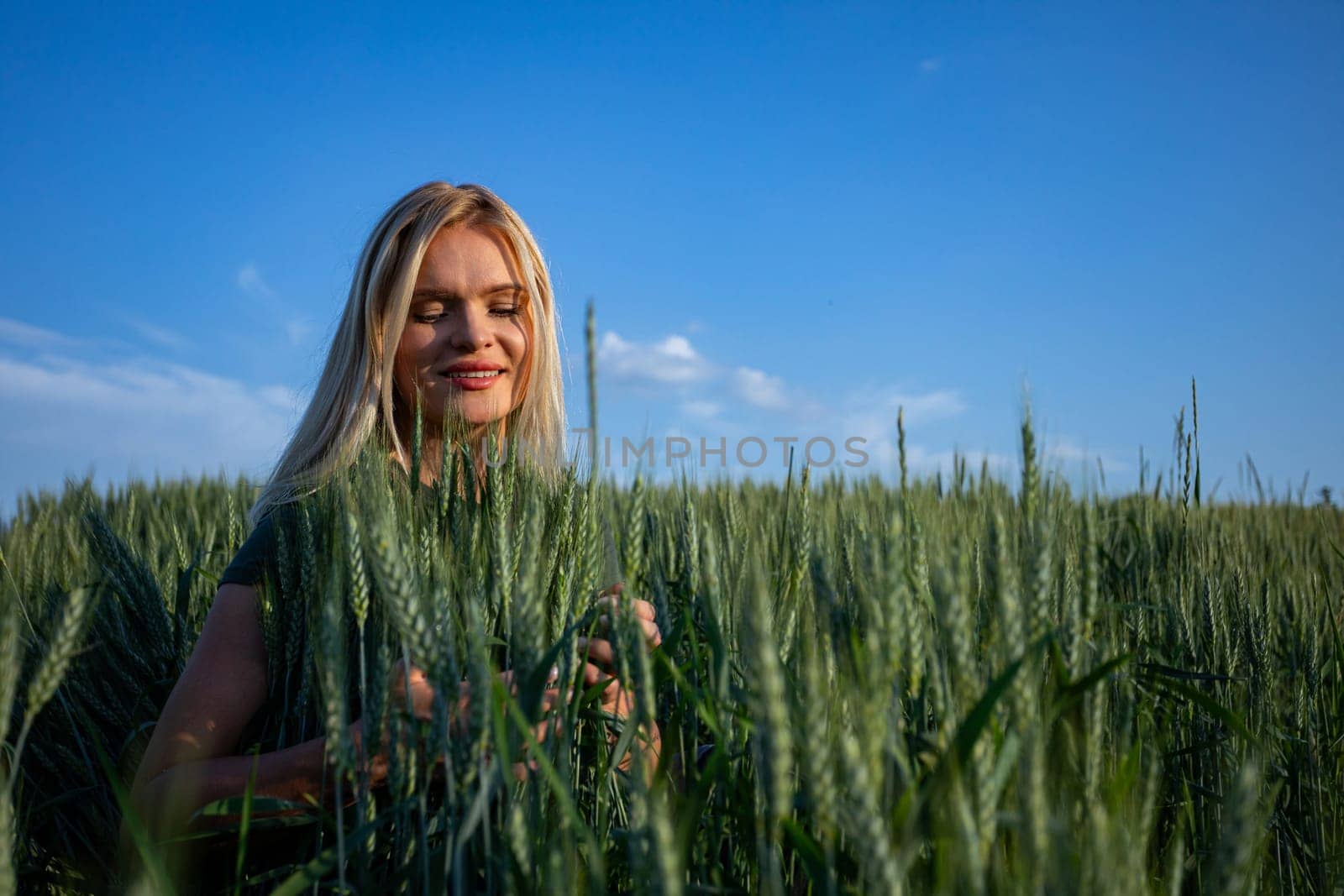 On a sunny day, a young and attractive female farmer stands proudly in her wheat field, overseeing her bountiful crops. Dressed in practical work attire, her blonde hair catching the sunlight, she exudes a sense of vitality and dedication. With a warm smile revealing her pearly white teeth, she radiates contentment and satisfaction. The wheat stalks tower around her, almost reaching her height, their vibrant green hue a striking contrast against the blue sky. As she surveys the golden expanse before her, her satisfaction with the abundant harvest is evident. Against the backdrop of the sunlit landscape, her presence adds a touch of rural charm to the scene. This captivating image captures the essence of agricultural life, where hard work and perseverance yield fruitful rewards, and the beauty of nature is celebrated with every successful harvest