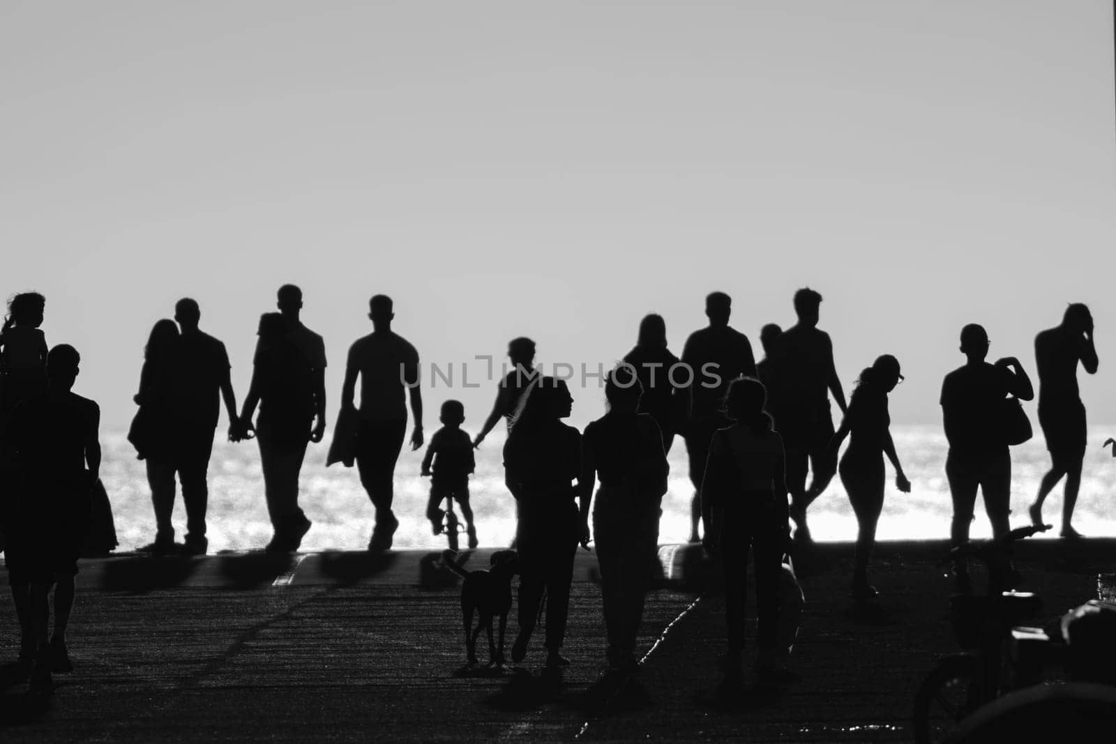 Monochrome image of silhouettes of people walking on the hill by the sea. Mid shot