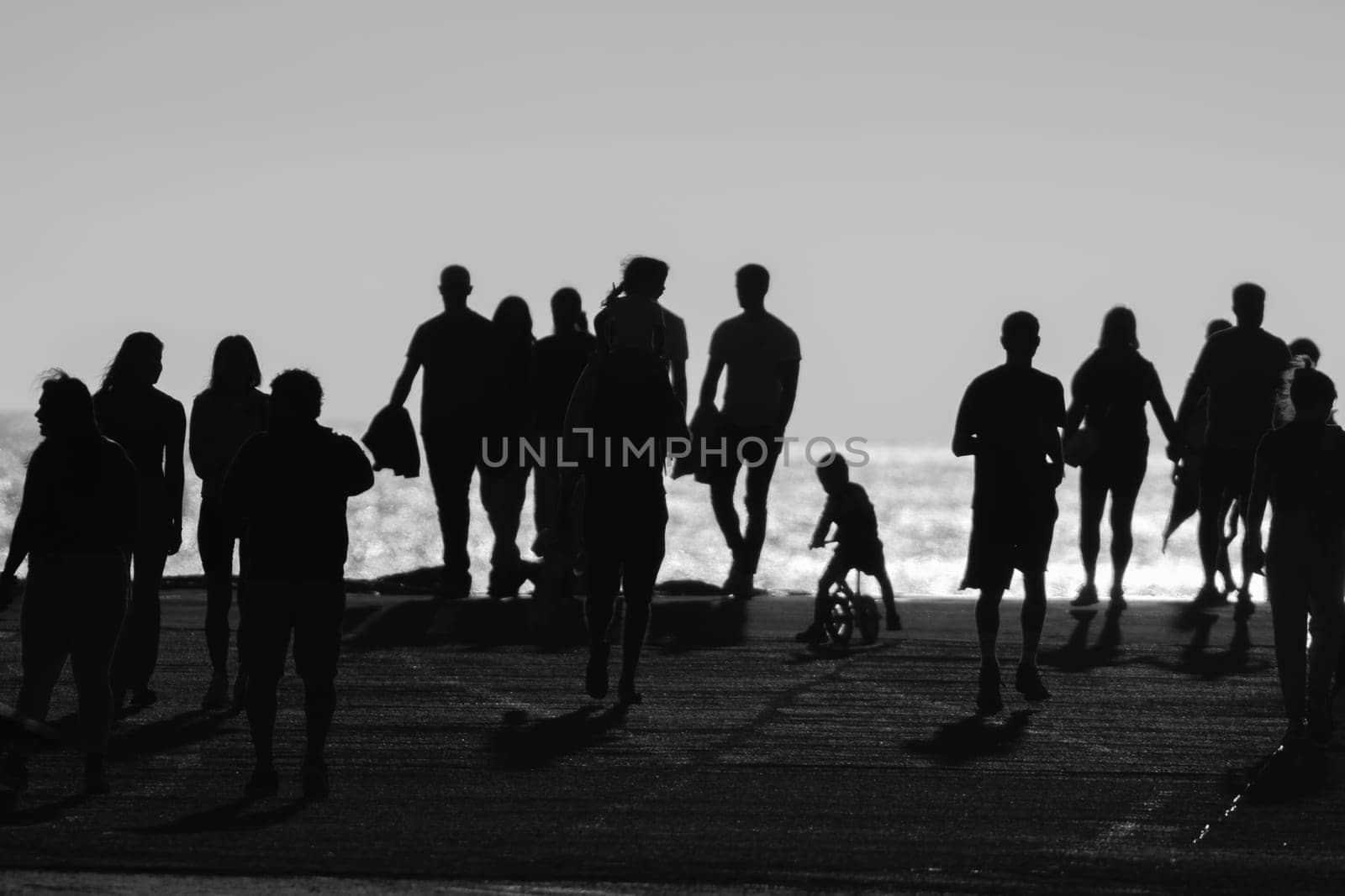 Monochrome image of silhouettes of people walking at sunset. Mid shot