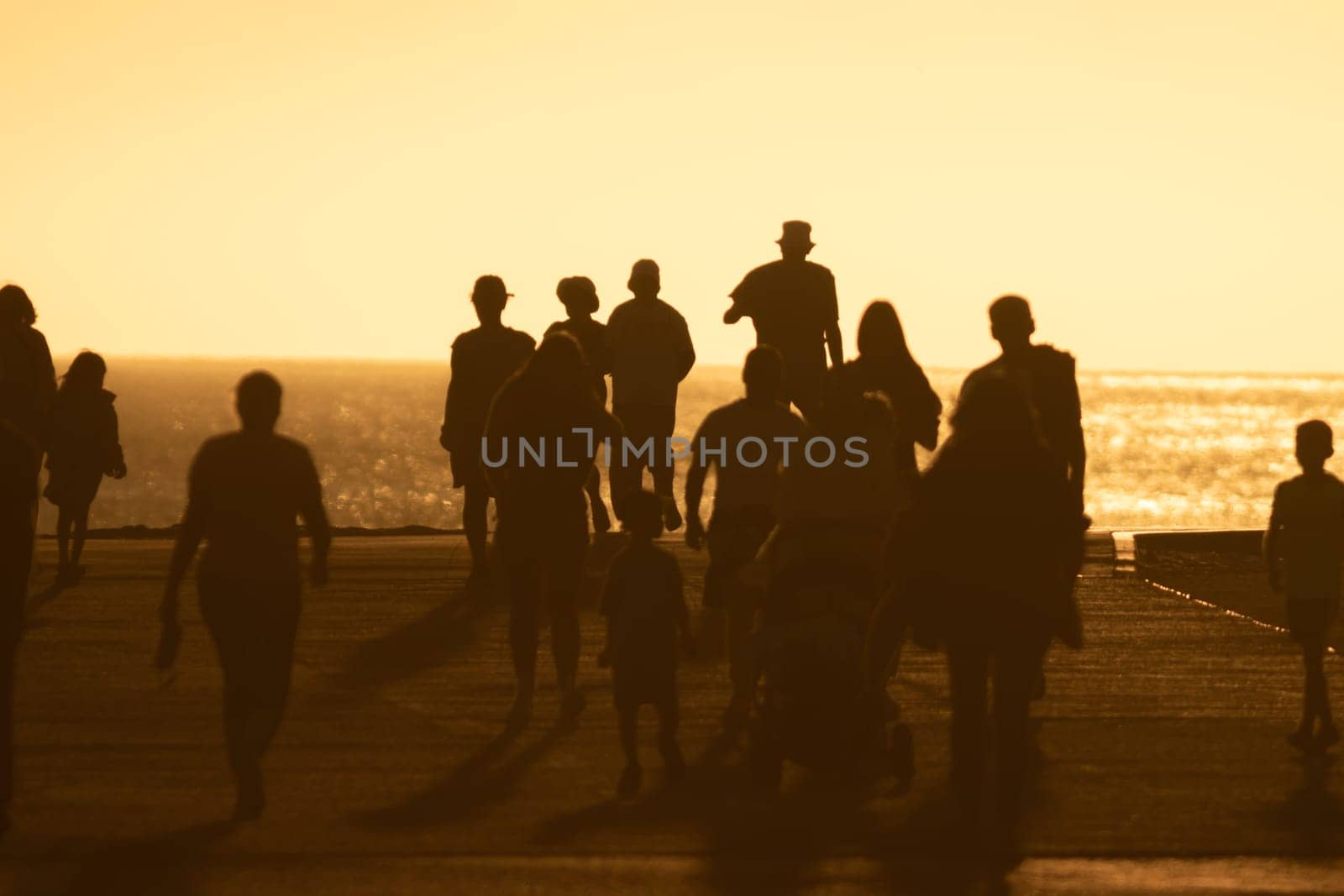 Silhouettes of people walking at yellow bright sunset. Mid shot