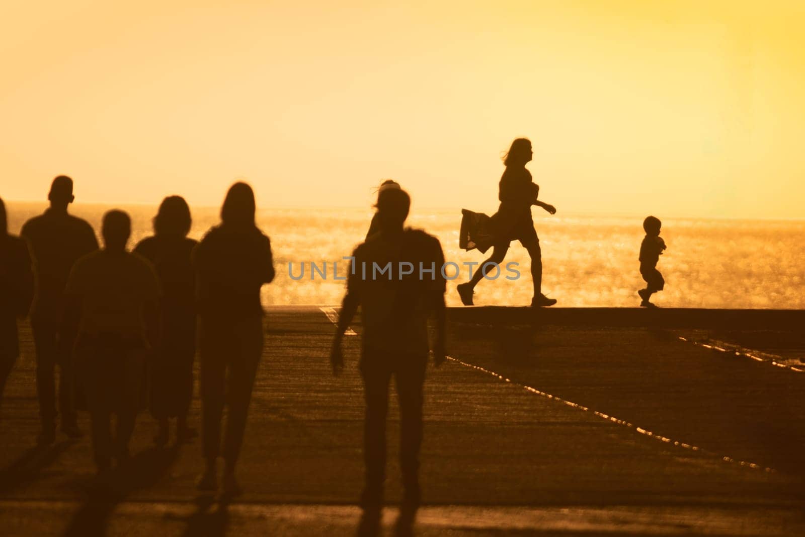 Silhouettes of people at yellow sunset - mother chasing her little baby. Mid shot