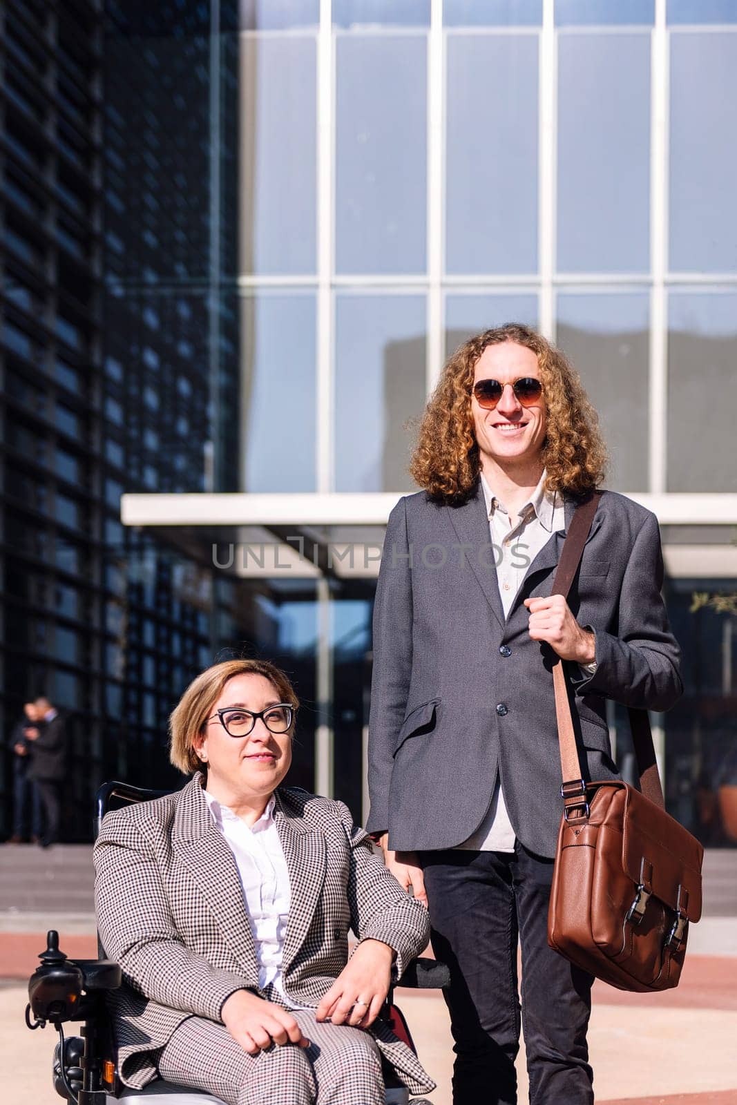 business man and woman using wheelchair smiling happy looking at camera outdoors at financial district, concept of diversity and urban lifestyle, copy space for text