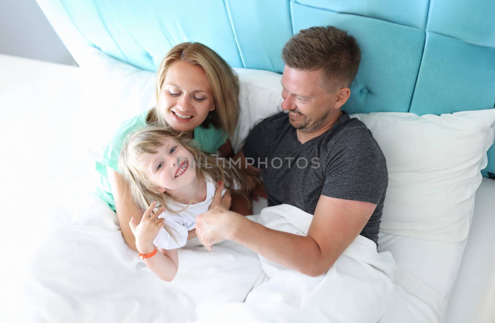 Parents with child indulge and cuddle in bed by kuprevich