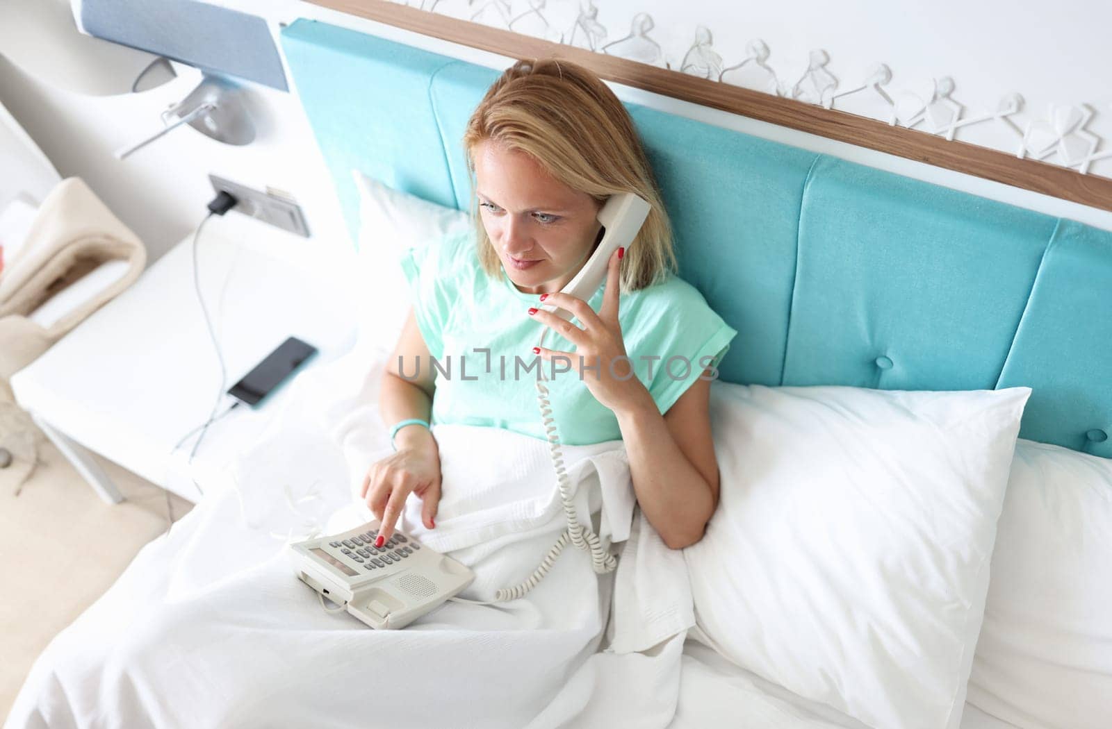 Woman lies on bed and dials number on phone. High-quality service in hotel rooms concept