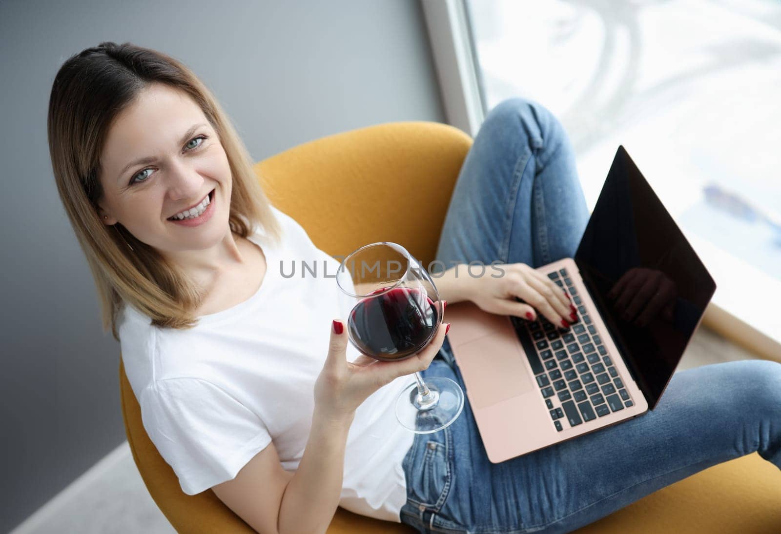 Woman with glass of wine sitting with laptop on her lap. Social media communication concept