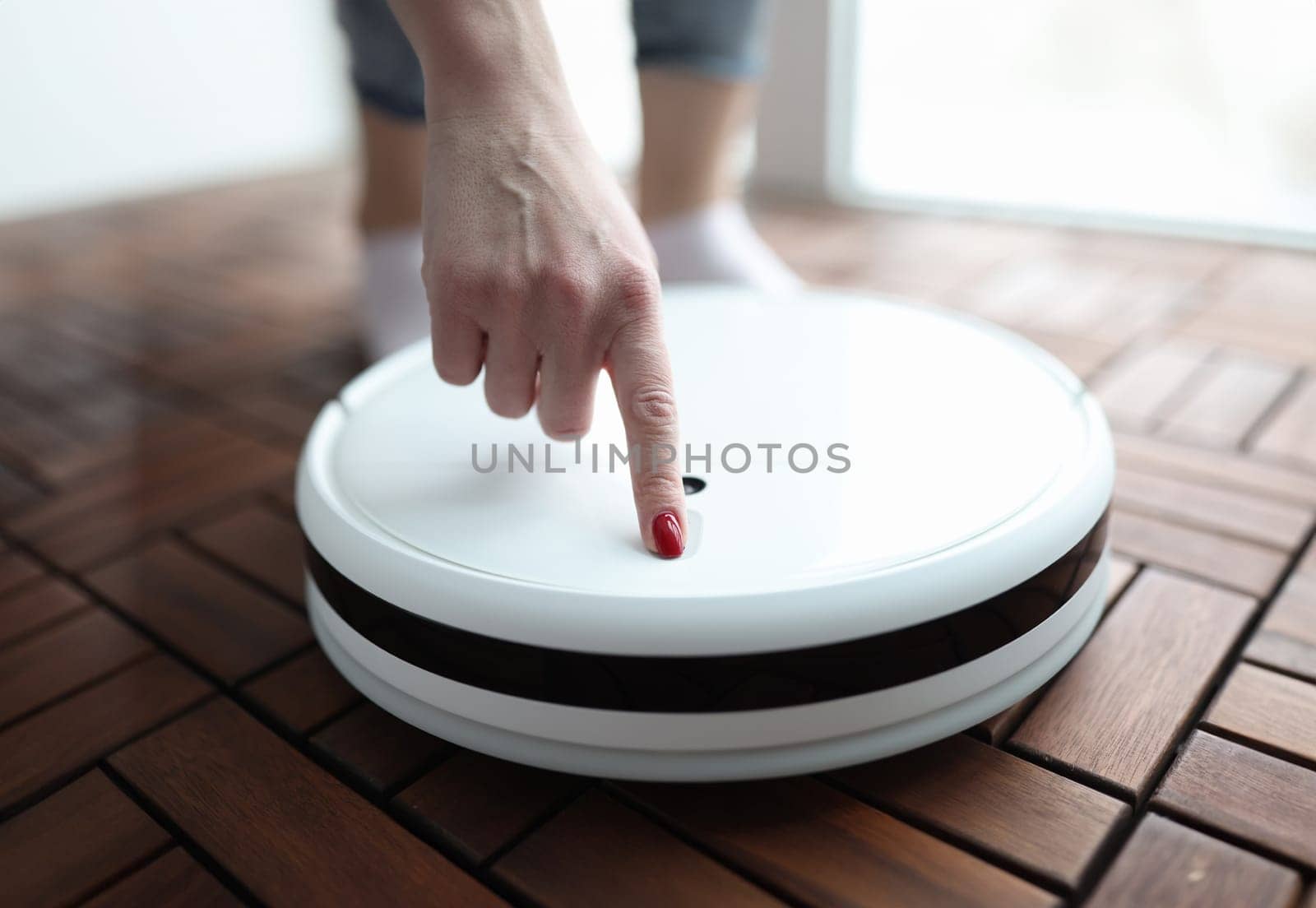 Woman pushing button in robot vacuum cleaner closeup by kuprevich