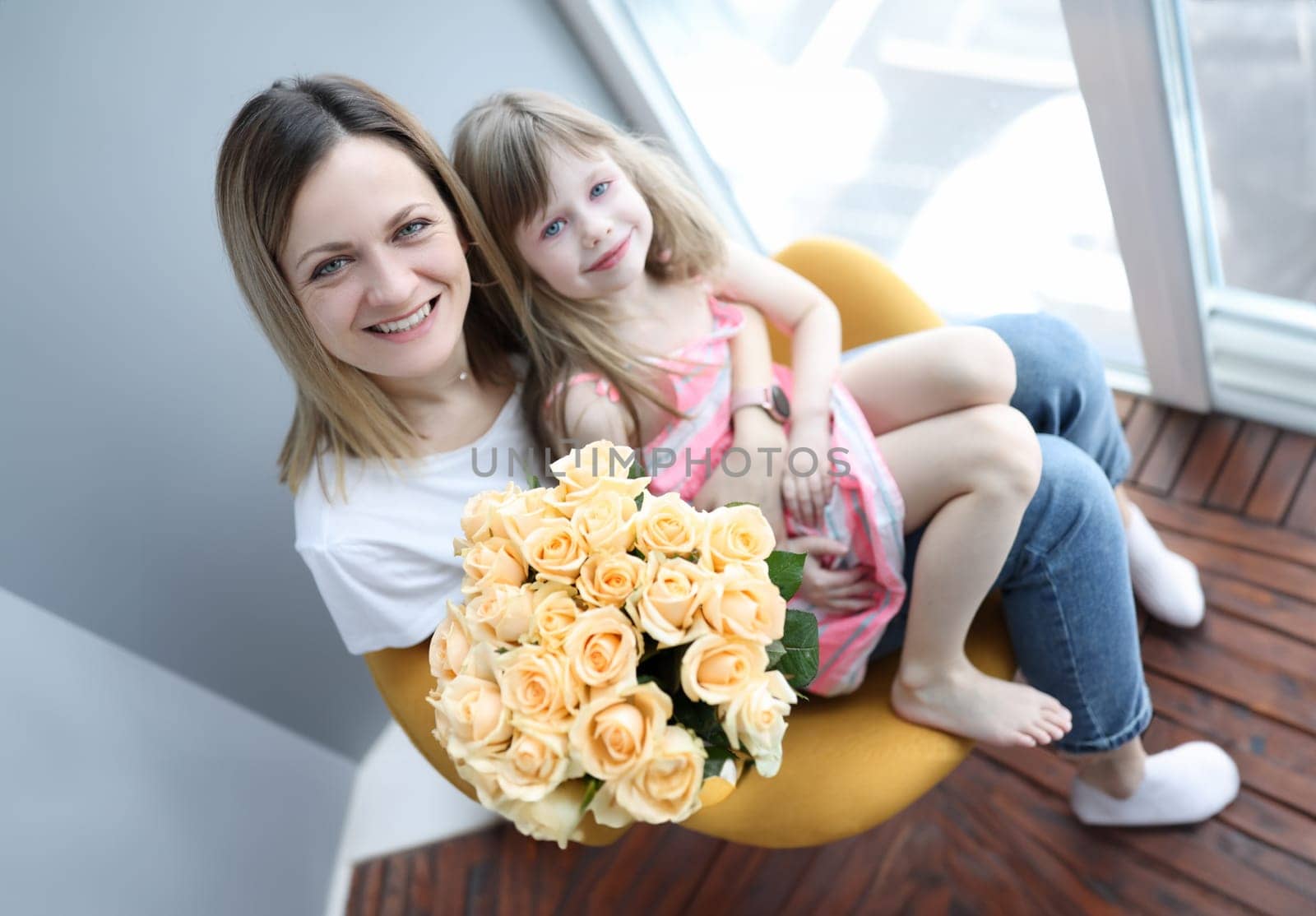 Woman with little girl on her knees holding bouquet of flowers. Mothers day concept