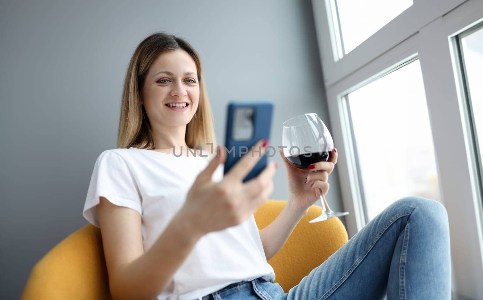 Woman with glass of wine looking at phone screen. Remote celebration concept