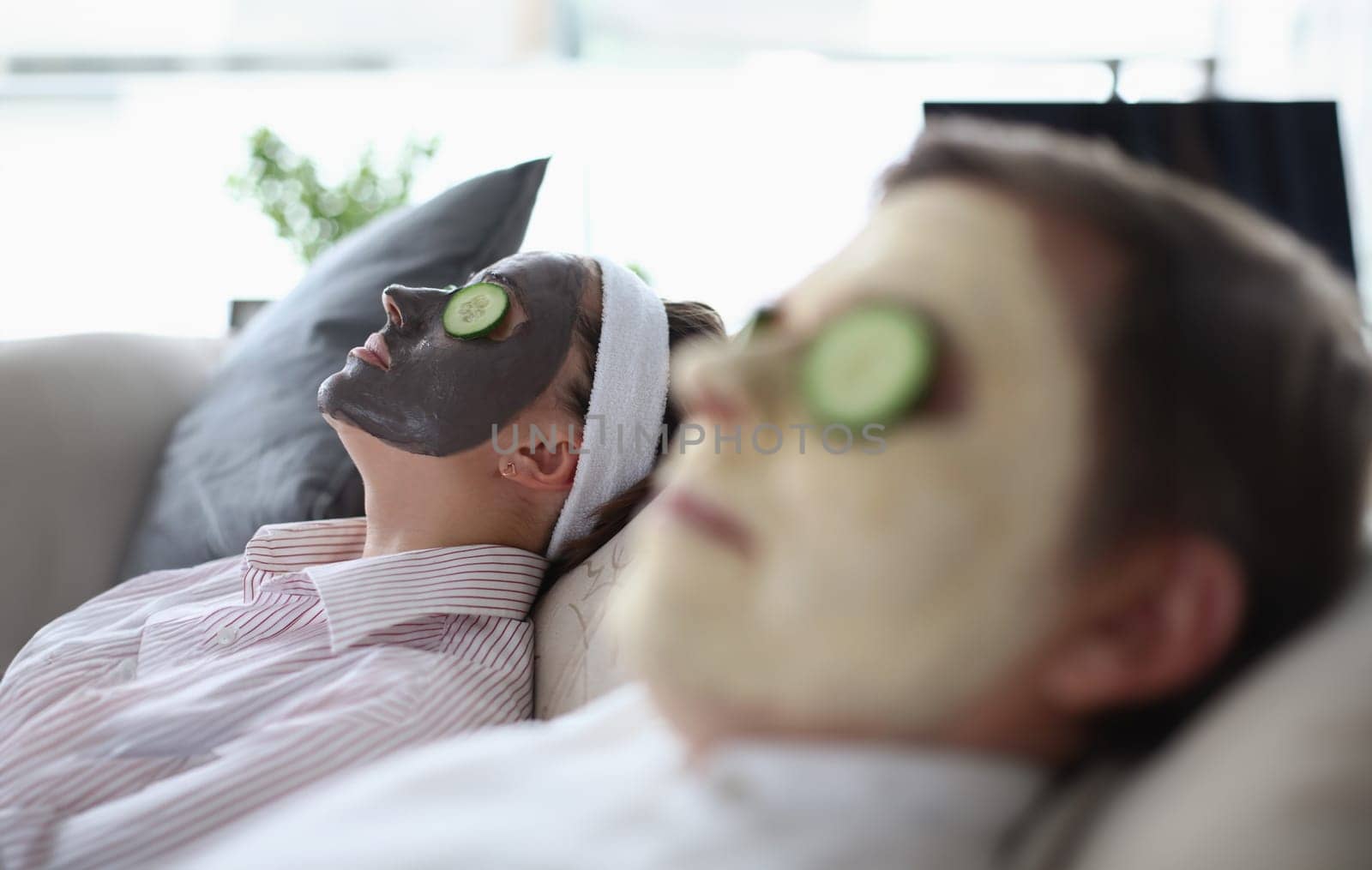 Man and a woman are lying on couch with rejuvenating mask on their face. Home treatments for facial rejuvenation concept