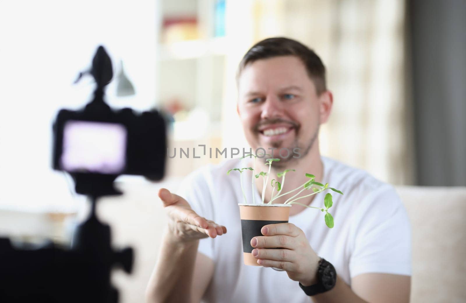 Smiling man demonstrates seedlings on video camera. Introducing home growing blog concept