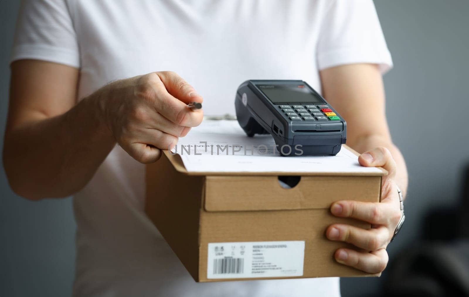 Courier holds cardboard box with payment terminal and documents with pen by kuprevich