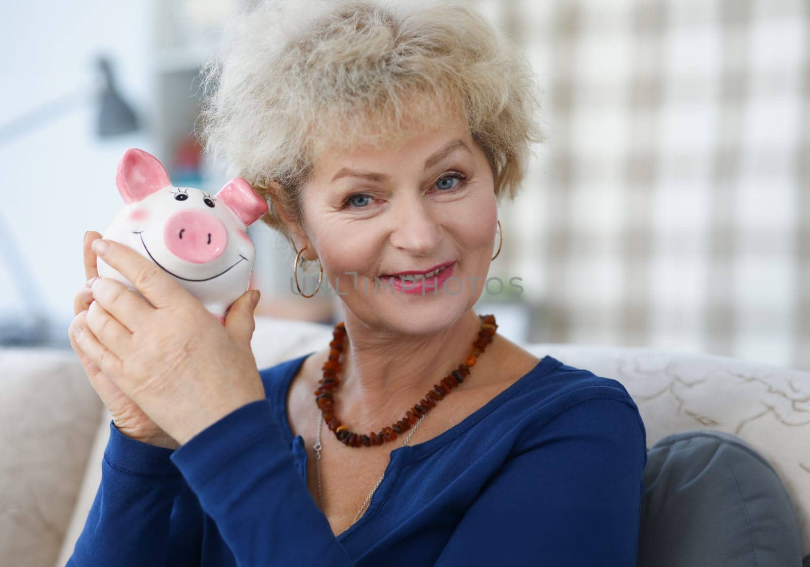 Portrait of an elderly woman who holds piggy bank in her hand by kuprevich