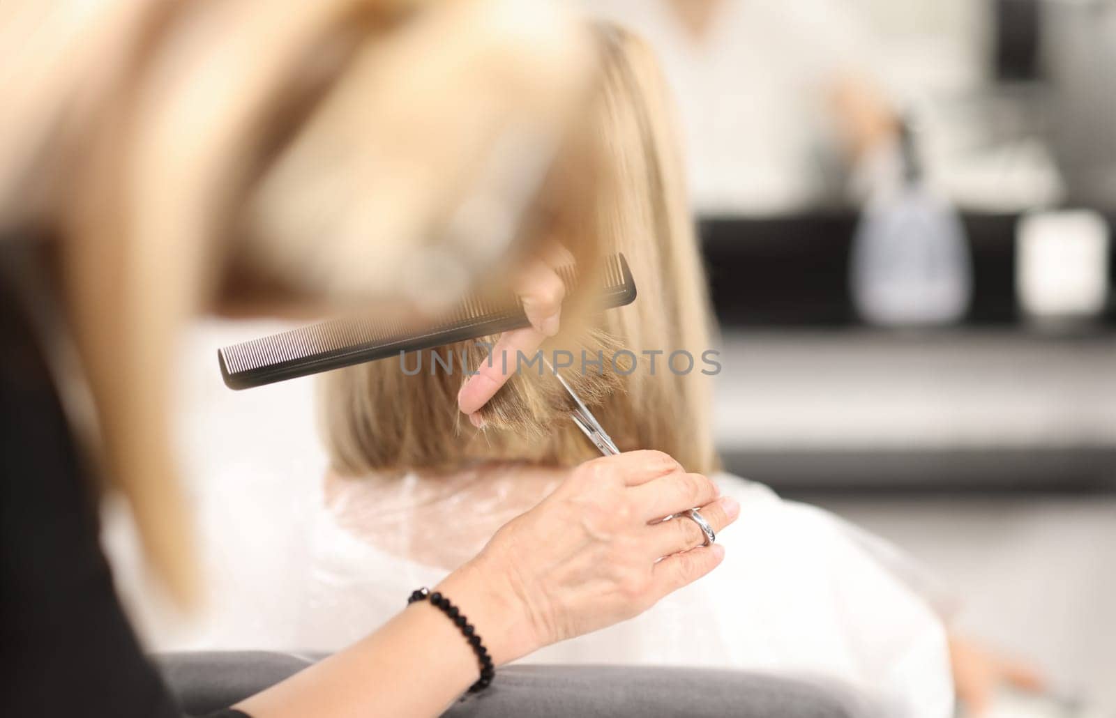 Hairdresser holds comb and scissors in his hands and cuts client's hair. Beauty salon services concept