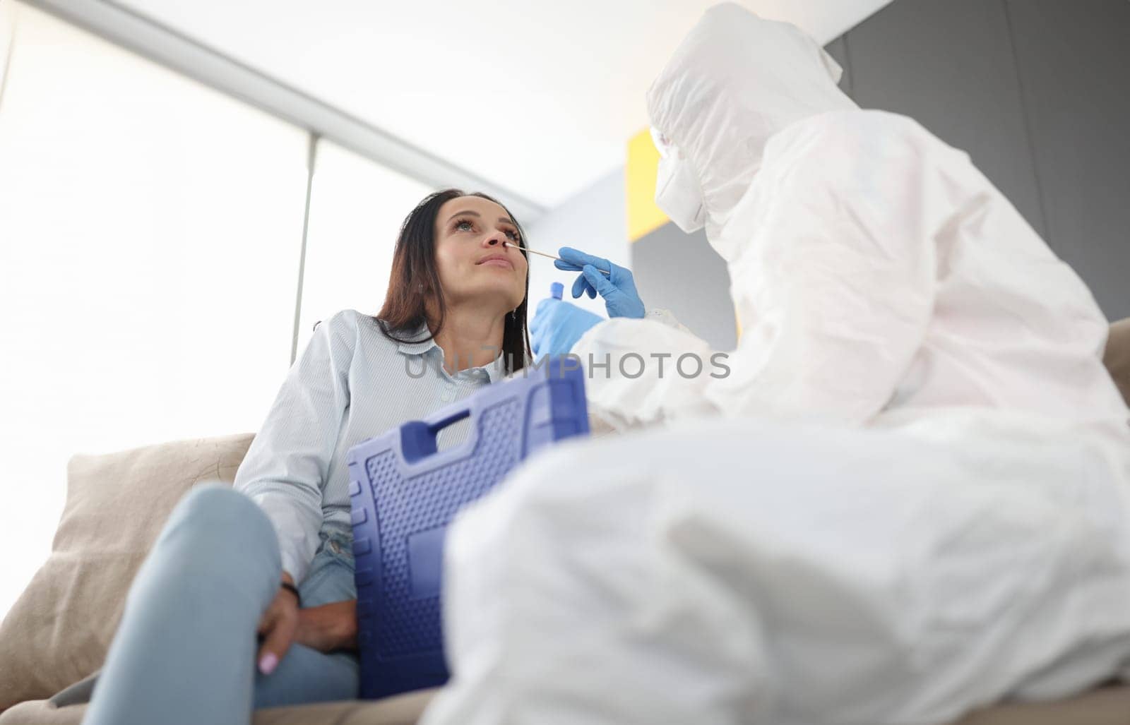 Doctor in protective suit is taken from woman with cotton swab. Taking material to determine coronavirus infection concept