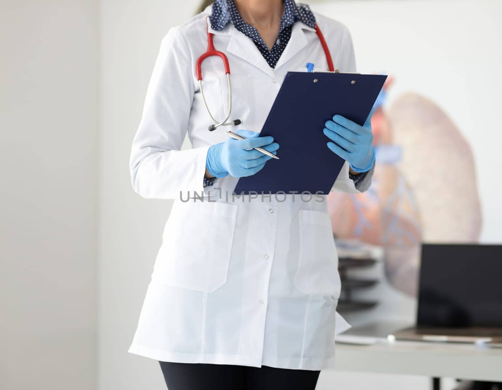 Doctor's hands in protective gloves hold clipboard and pen by kuprevich