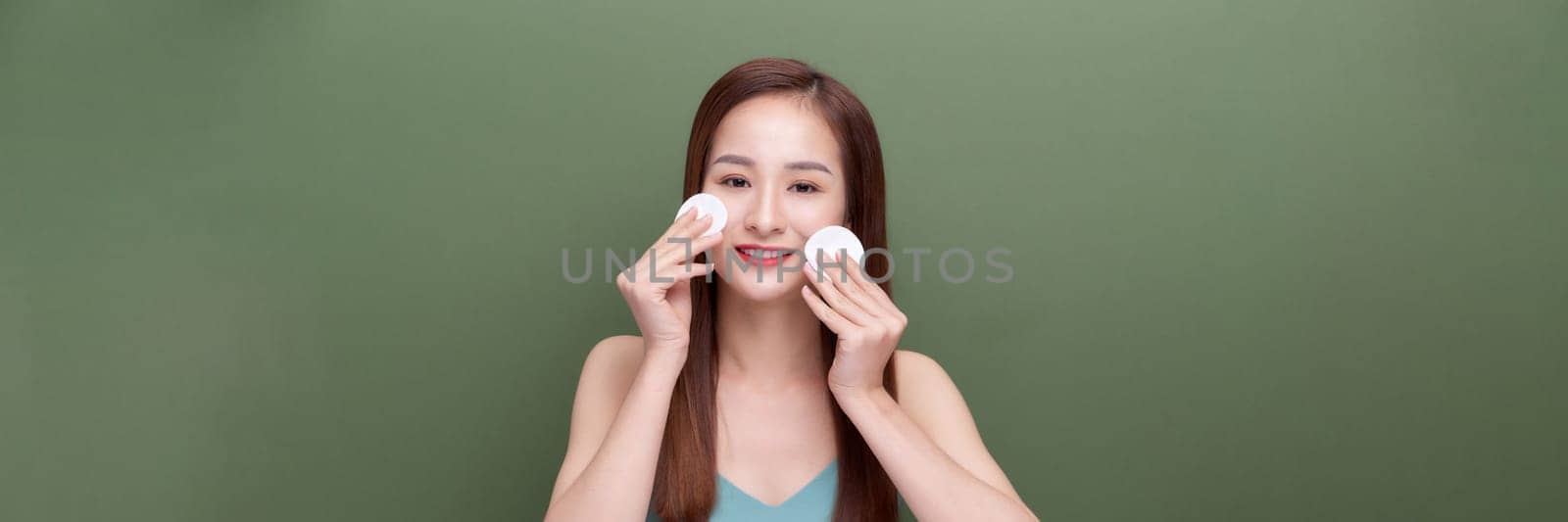 positive and naked woman holding cotton pad near face isolated on green, panorama, crop