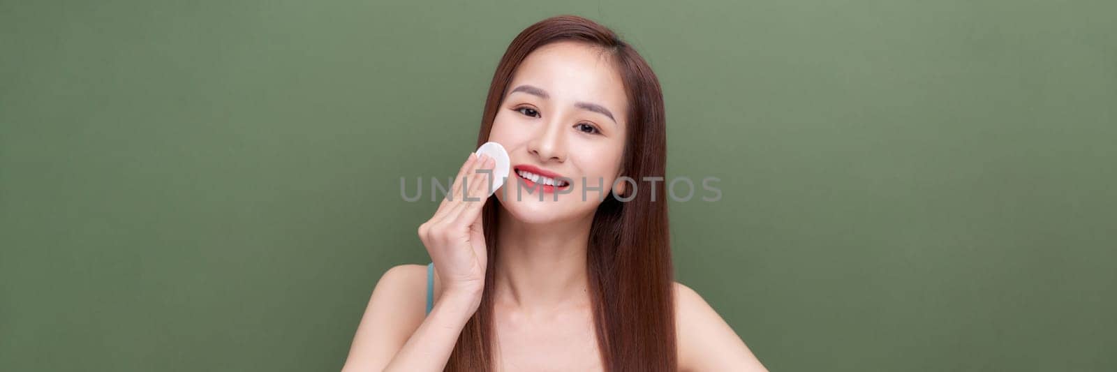 attractive smiling woman cleaning skin on green banner background by makidotvn