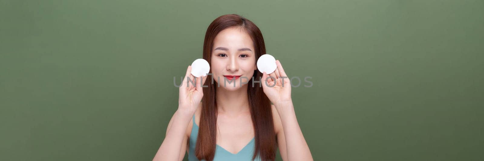 Girl applying lotion using cotton pad over green background, panorama, crop by makidotvn