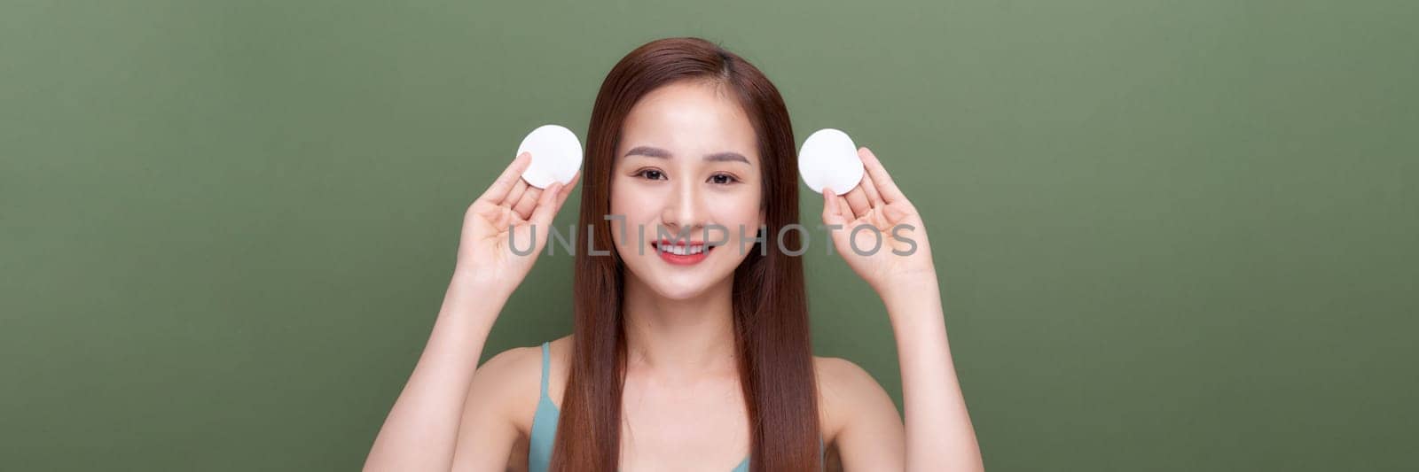 positive and naked woman holding cotton pad near face isolated on green, panorama, crop