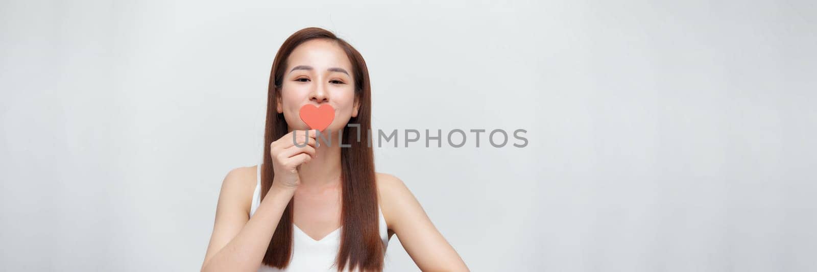 Woman in love, holding a little paper heart over eye, standing over white background, panorama by makidotvn
