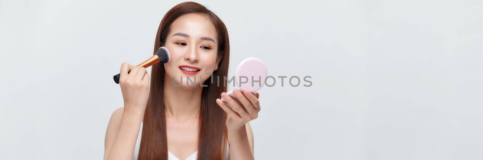 beautiful happy young girl with perfect skin is holding makeup brush in hand over banner background by makidotvn