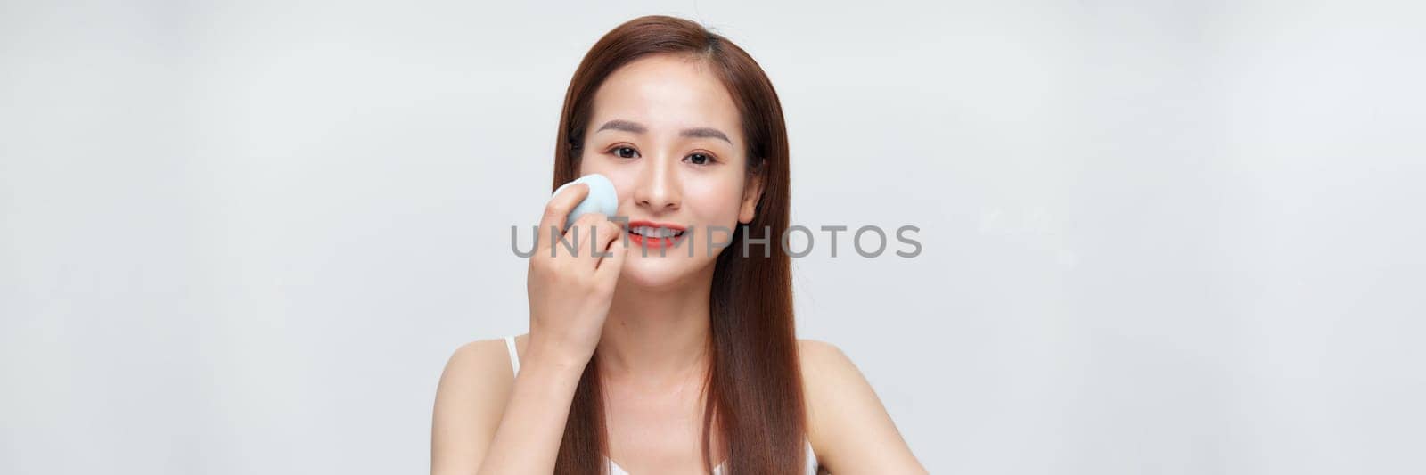 Beautiful young woman applying makeup using beauty blender sponge. by makidotvn