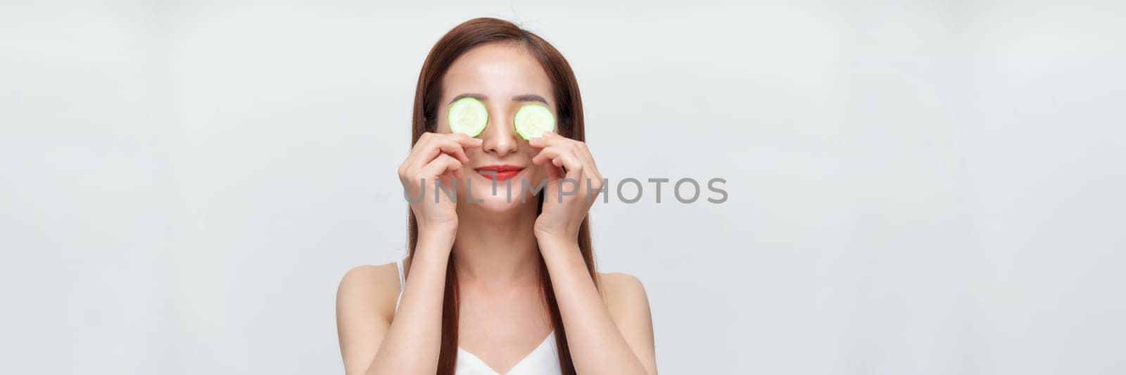 woman making eye mask of cucumbers over white banner by makidotvn