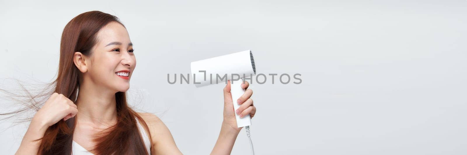 Woman dries her beautiful long hair with a hair dryer against a white background. Web banner