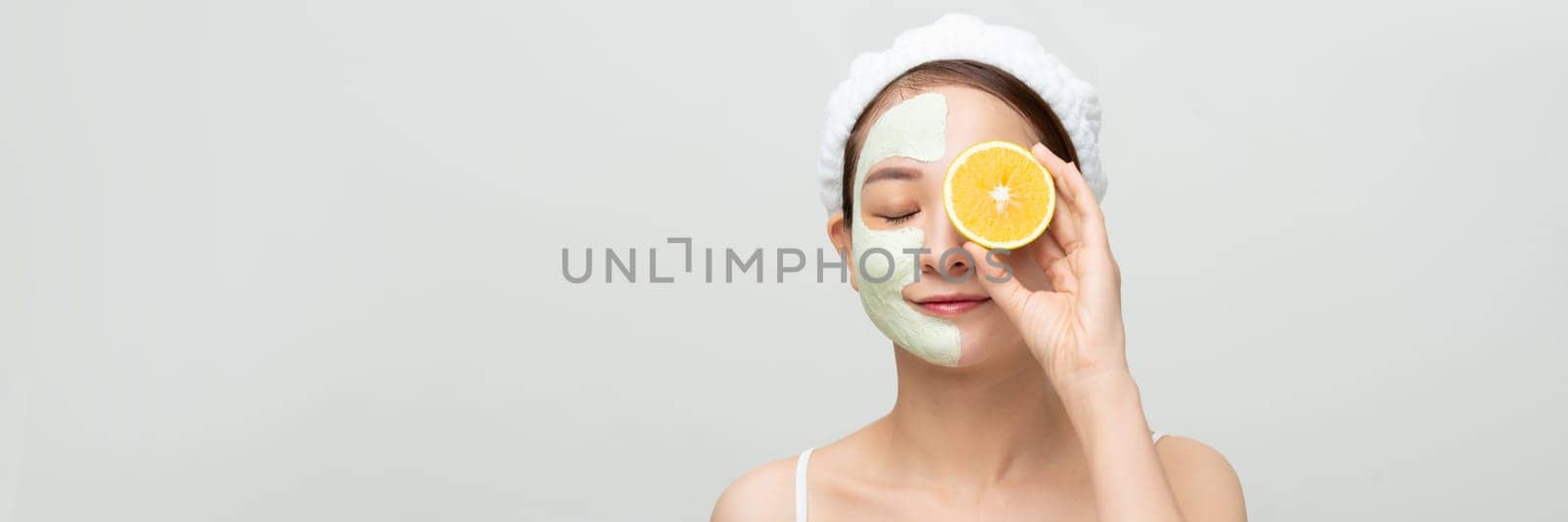 Banner with beautiful happy girl applying mud mask showing a juicy orange on white