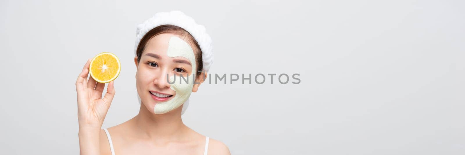 Emotional young woman with facial mask and halves of ripe orange on white background. Web banner. by makidotvn